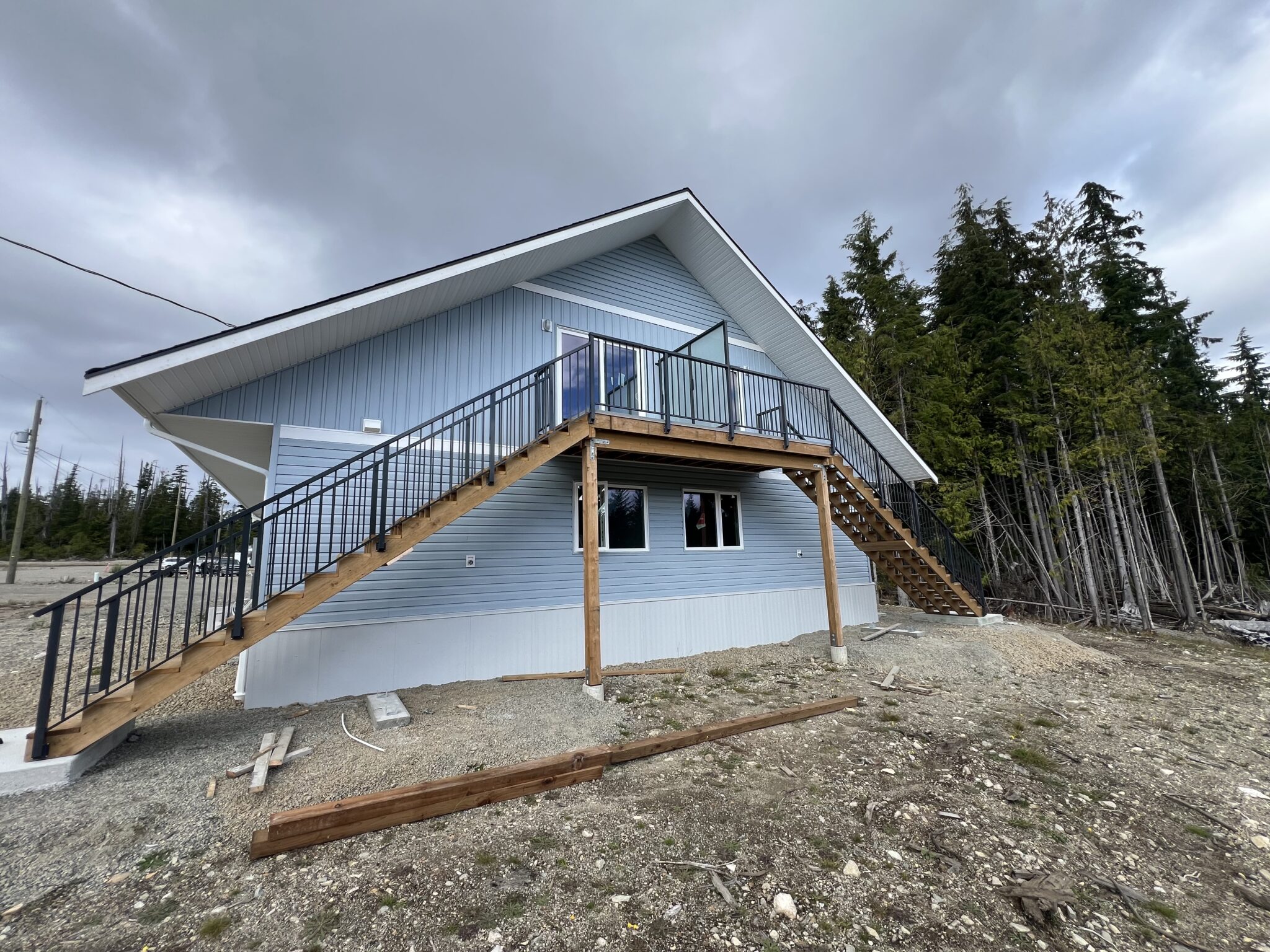 Exterior staircase on a Bamfield home fitted with black aluminum railings along both sides, connecting to an upper deck on a blue-sided house.