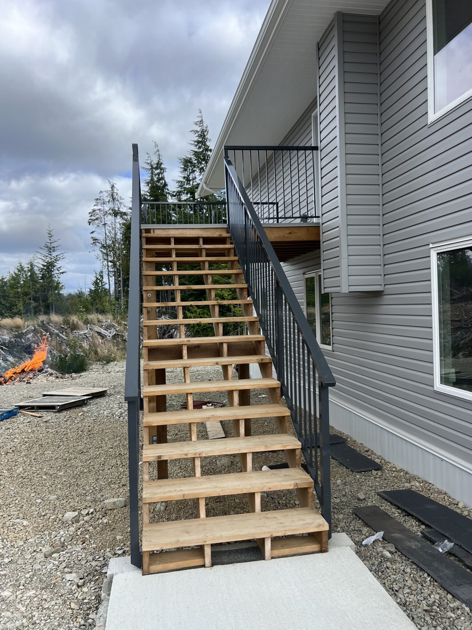 A wooden staircase at a Bamfield property finished with durable black metal railings, ascending to an upper entry door.