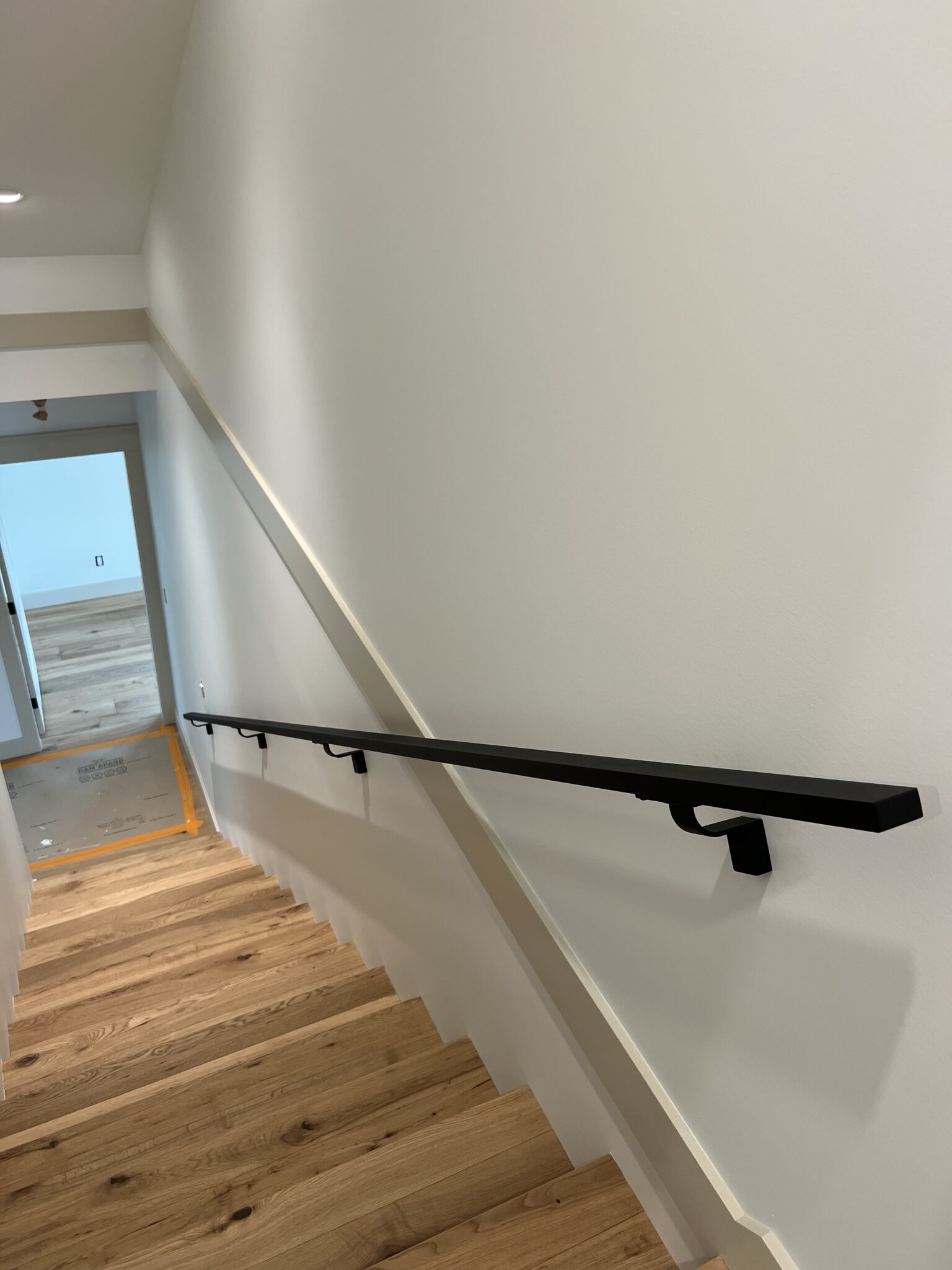 Black aluminum railings in Nanoose Bay home mounted on a white wall beside a wooden staircase, shown from the top looking downward toward a hallway.