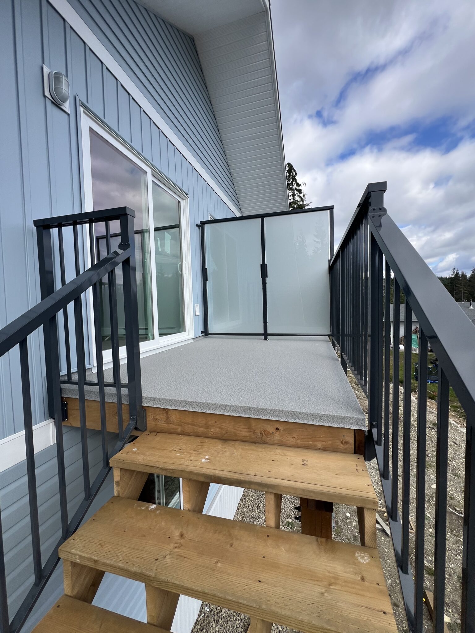 Black aluminum railings lining a set of wooden outdoor stairs in Bamfield, leading up to a small landing beside a sliding gate door.